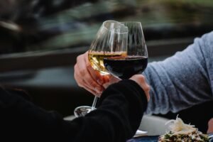 A couple clinking red and white wine glasses during an intimate outdoor moment.